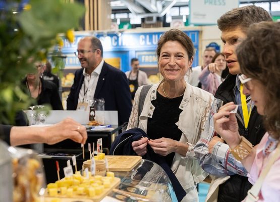 Trade show attendees tasting and exploring gourmet food products at an exhibitor booth, with product presentations and discussions around showcased innovations.