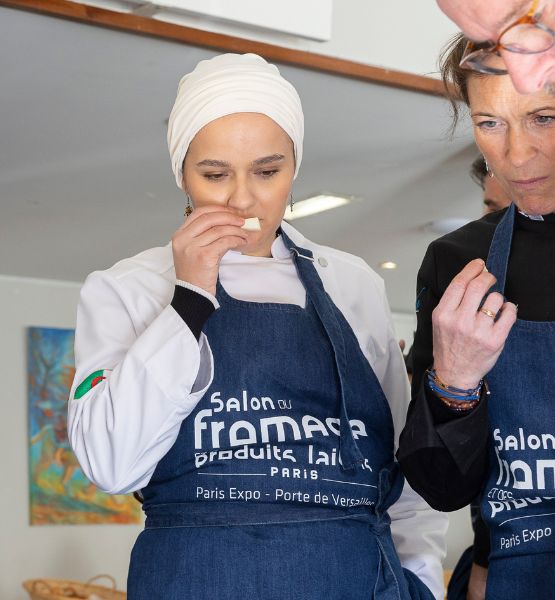 Professional in a Salon du Fromage apron tasting a dairy product during a food event.