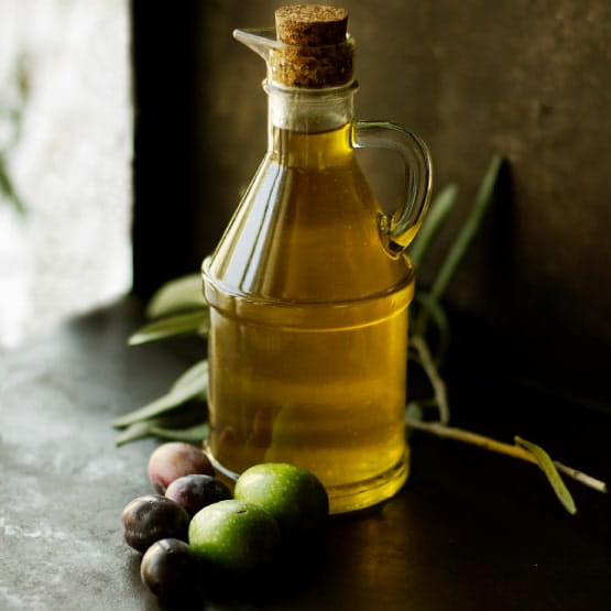 Bouteille d'huile d'olive avec des olives autour. 