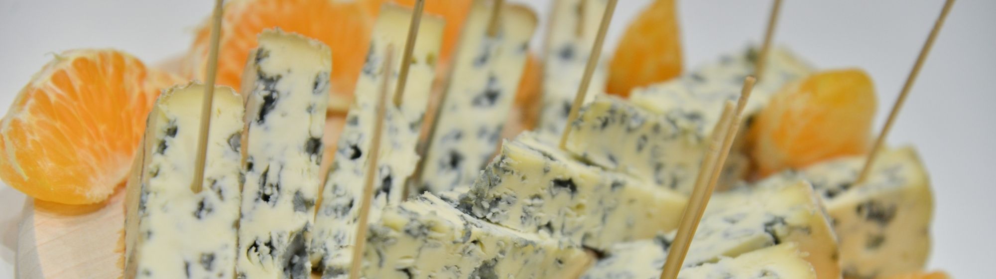 Plate of blue cheese slices with wooden picks and mandarin segments around.