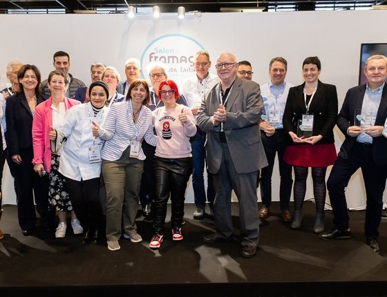 Group of people at the cheese salon, holding 'Coup de Cœur 2024' awards, holding trophies in their hands