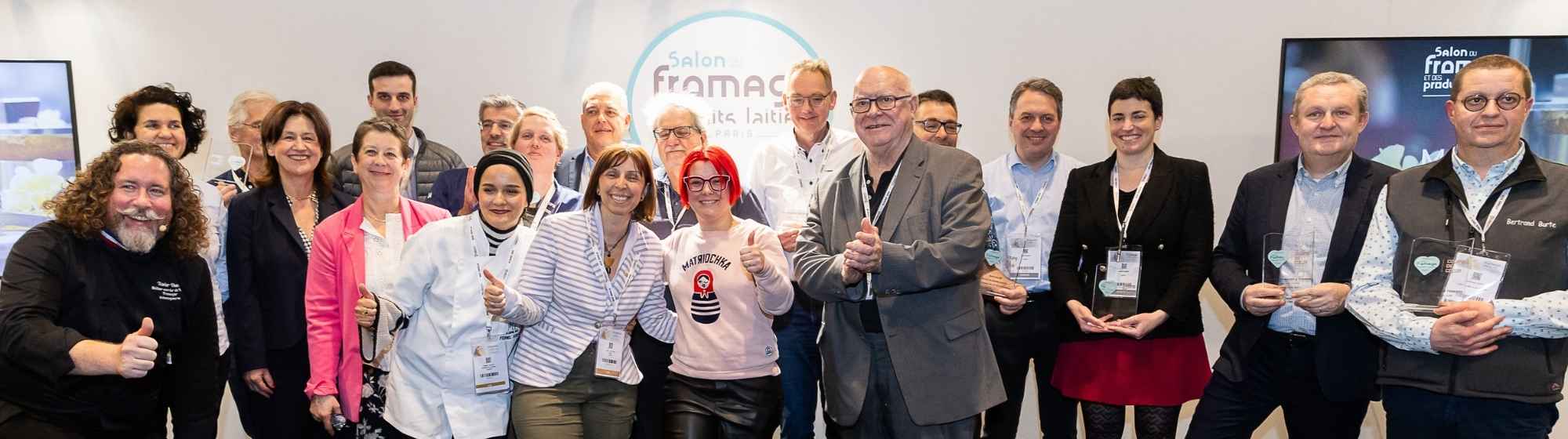 Group of people at the cheese salon, holding 'Coup de Cœur 2024' awards, holding trophies in their hands